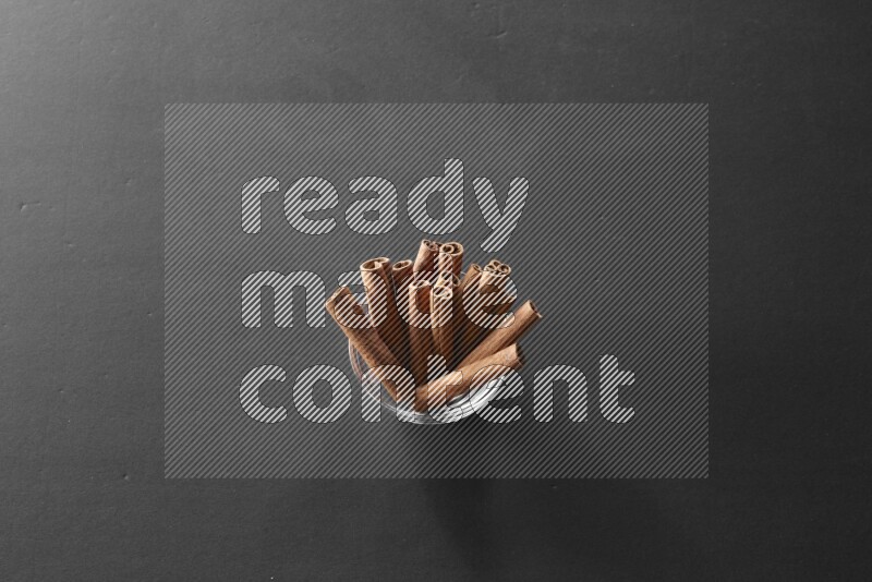 A glass bowl full of cinnamon sticks on black flooring
