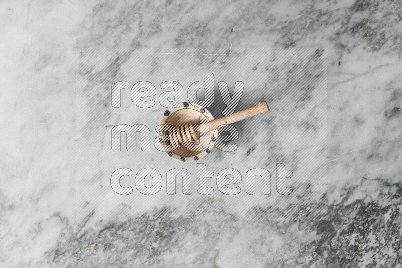 Decorative pottery bowl with wooden honey dipper in it on grey marble background