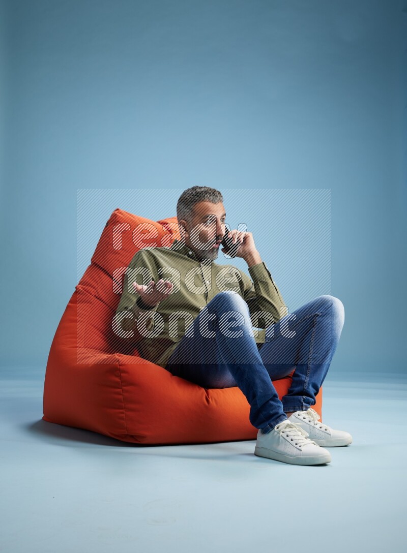 A man sitting on an orange beanbag and talking on the phone