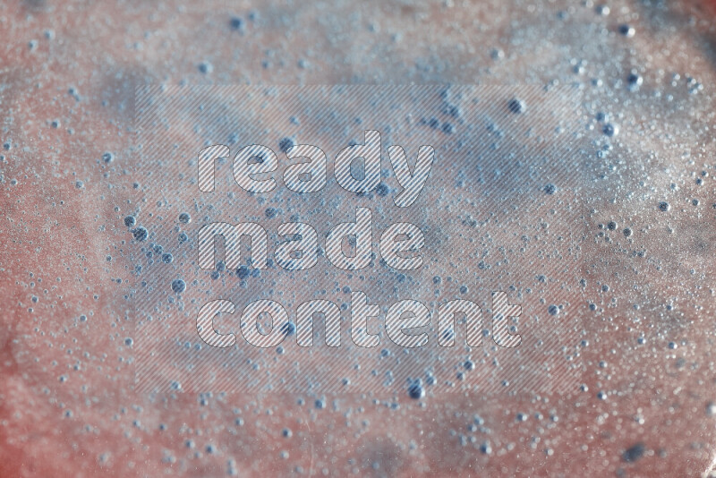 لقطات مقربة لقطرات ألوان مائية زرقاء على سطح الزيت على خلفية حمراء