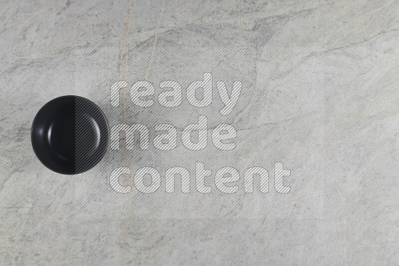 A black ceramic bowl on grey marble background