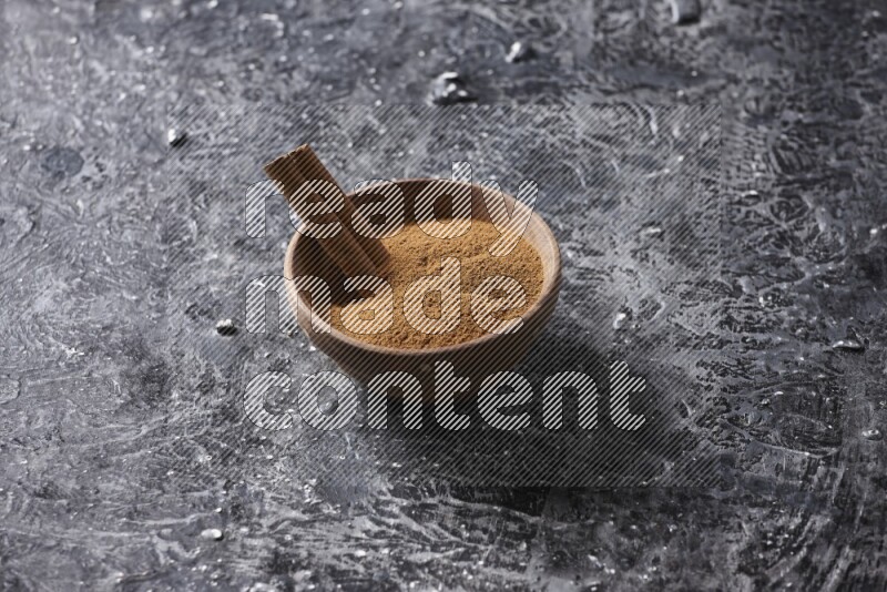 Wooden bowl full of cinnamon powder and a cinnamon stick on a textured black background