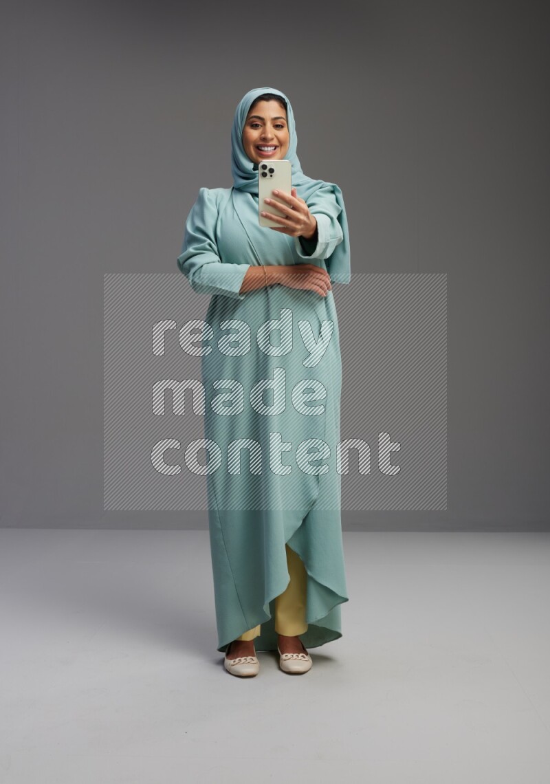 Saudi Woman wearing Abaya standing taking selfie on Gray background