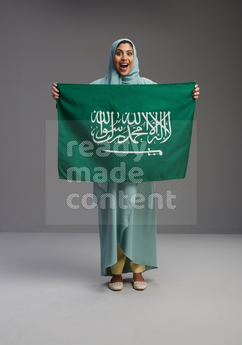 Saudi Woman wearing Abaya standing holding Saudi flag on Gray background