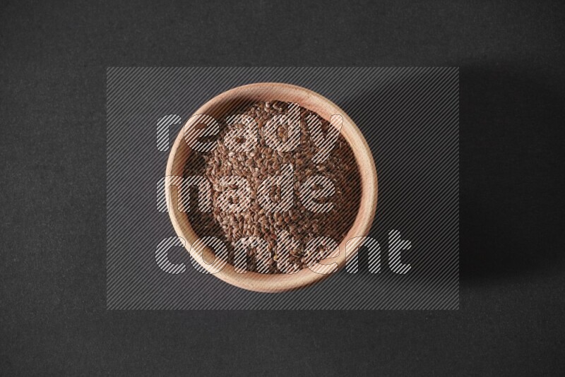 A wooden bowl full of flaxseeds on a black flooring