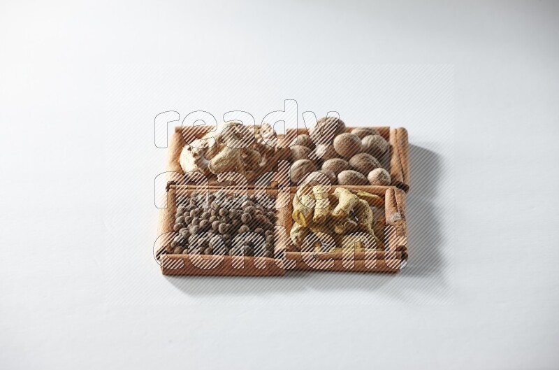 4 مربعات من أعواد القرفة ممتلئة بجوزة الطيب والزنجبيل المجفف وأصابع الكركم وبهار الفلفل الحلو على أرضية بيضاء