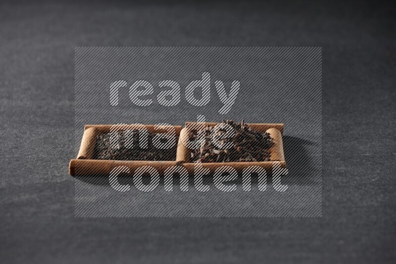 مربعان من أعواد القرفة ممتلئان بالشاي وحبوب القرنفل علي خلفية سوداء