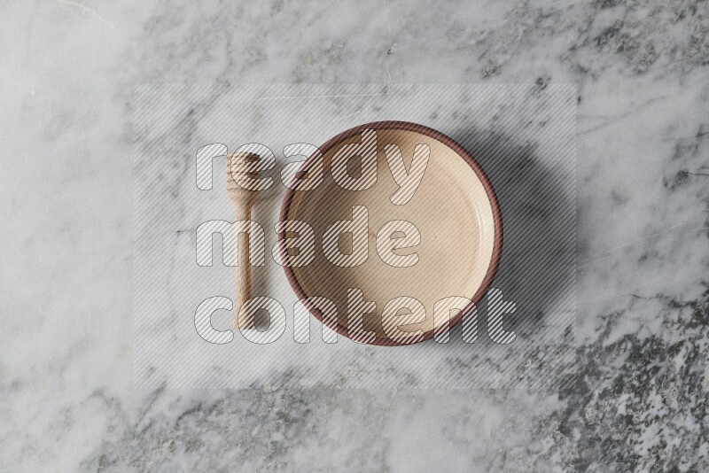 Beige pottery oven bowl with wooden honey dipper on the side on grey marble background