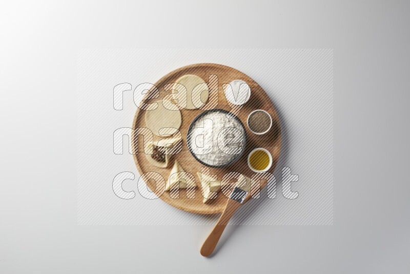 two closed sambosas and one open sambosa filled with meat while flour, salt, black pepper and oil with oil brush aside in a wooden dish on a white background