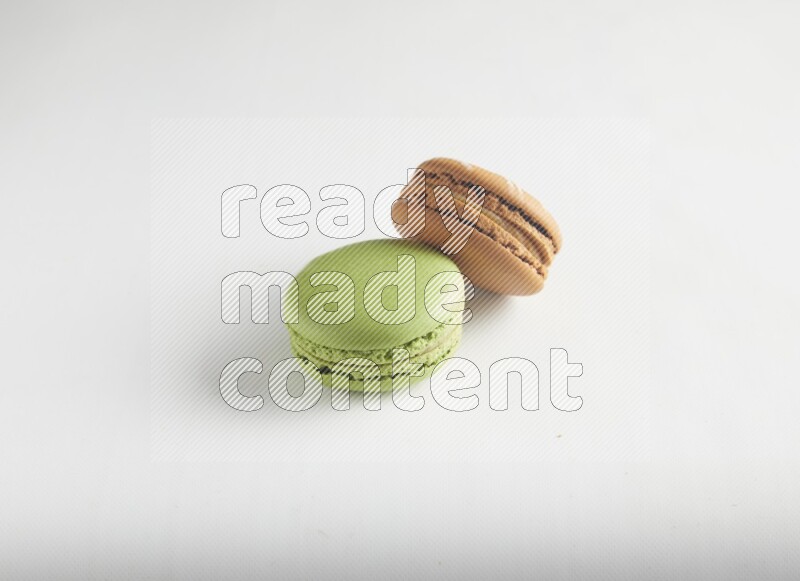 45º Shot of of two assorted Brown Irish Cream, and Green Pistachio macarons on white background