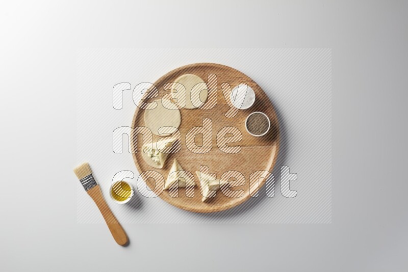 two closed sambosas and one open sambosa filled with cheese while salt, black pepper and oil with oil brush aside in a wooden dish on a white background