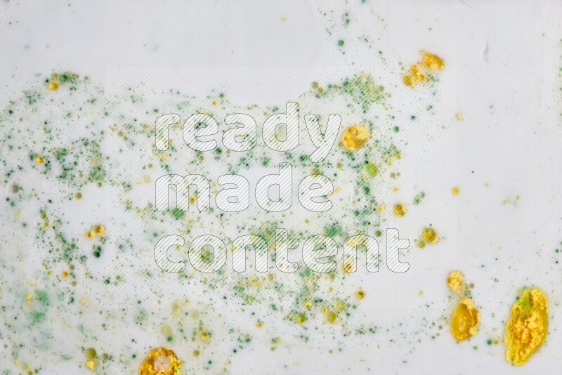 The image captures a splatter of yellow and green paint over a white backdrop