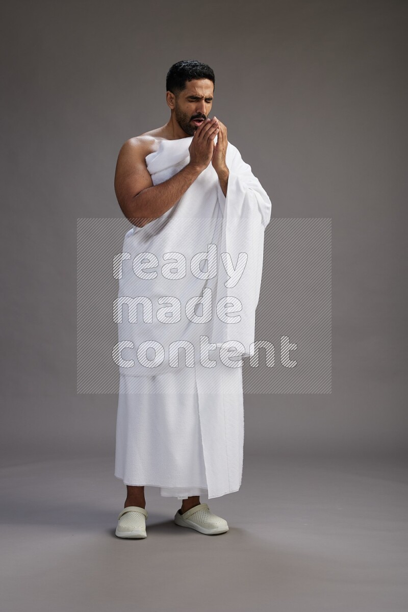 A man wearing Ehram standing showing how to sneeze on gray background