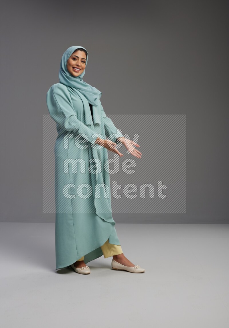 Saudi Woman wearing Abaya standing interacting with the camera on Gray background