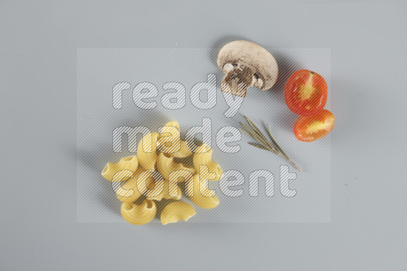 Raw pasta with different ingredients such as cherry tomatoes, garlic, onions, red chilis, black pepper, white pepper, bay laurel leaves, rosemary, cardamom and mushrooms on light blue background