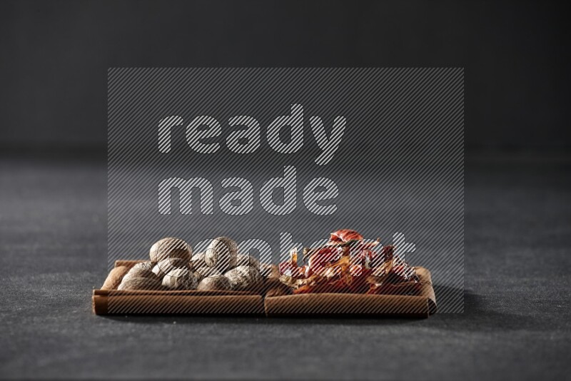 مربعان من أعواد القرفة ممتلئان بجوزة الطيب والفلفل الحار المجفف علي خلفية سوداء