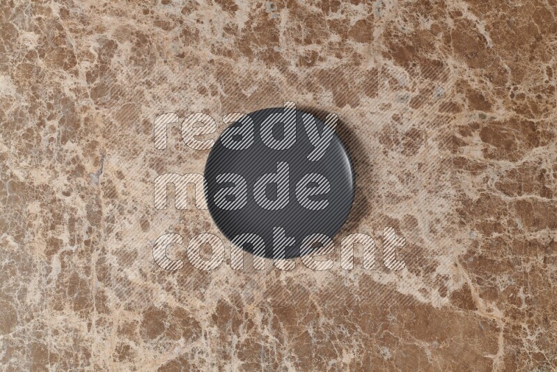 Top View Shot Of A Black Ceramic Circular Plate On beige Marble Flooring