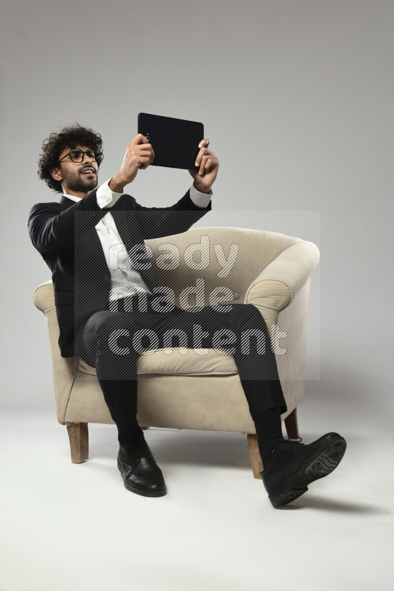 A man wearing formal sitting on a chair gaming on a tablet on white background