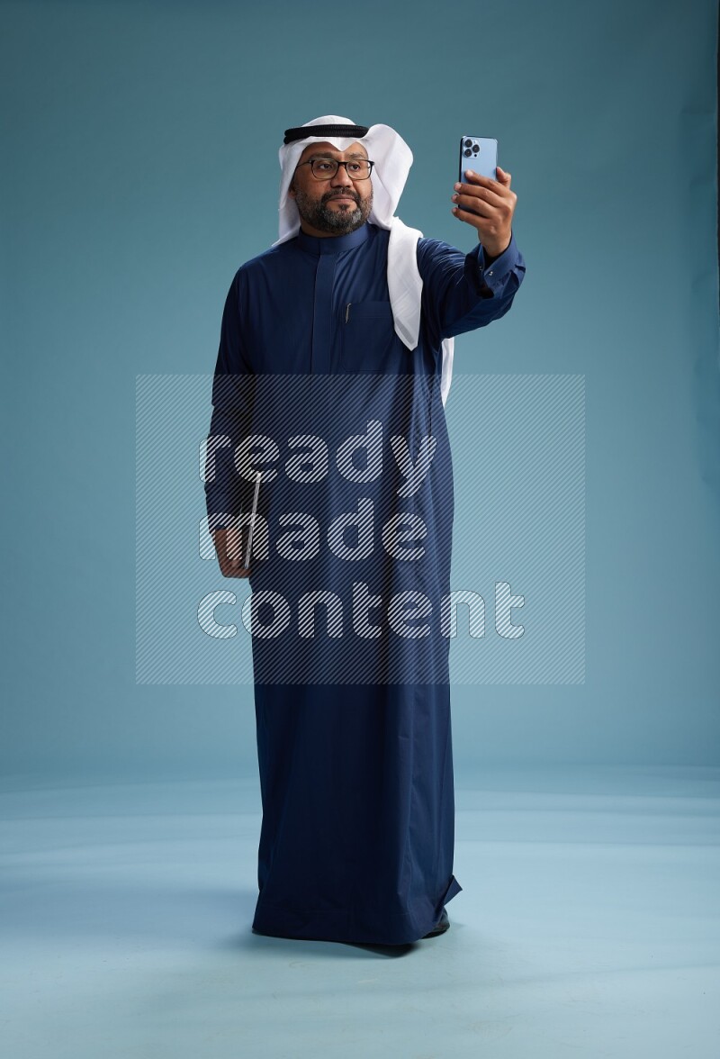 Saudi Man with shimag Standing taking selfie on blue background