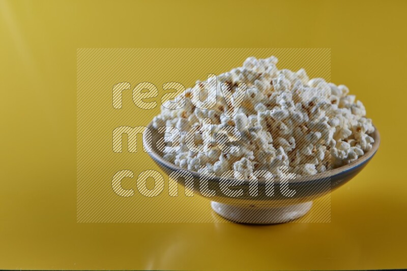 A multicolored ceramic plate full of popcorn on a yellow background in different angles