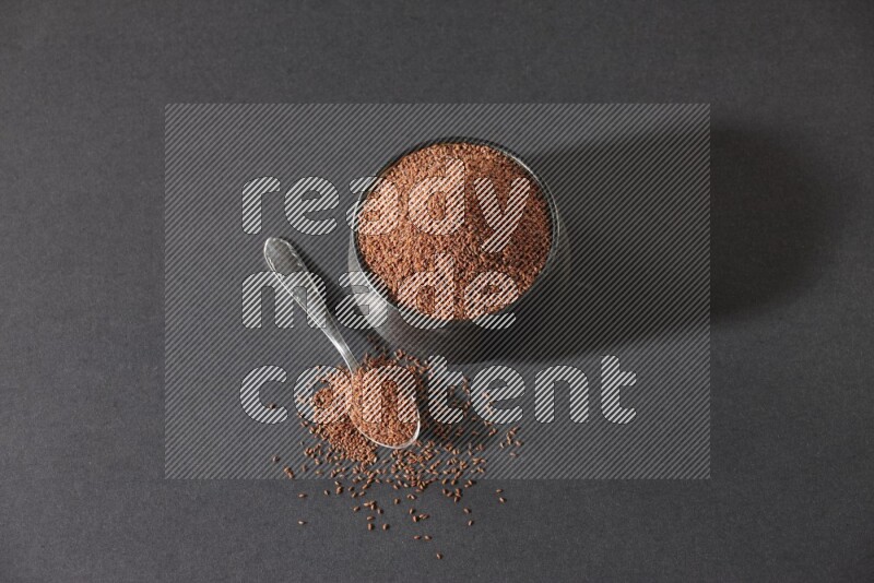 A black pottery bowl full of garden cress seeds and metal spoon full of the seeds on a black flooring