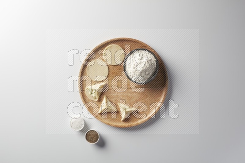 two closed sambosas and one open sambosa filled with cheese while flour, salt, and black pepper aside in a wooden dish on a white background