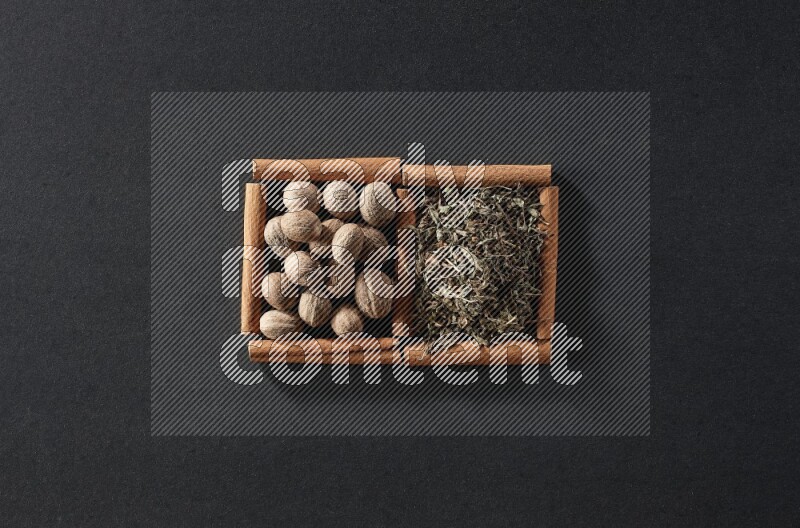 مربعان من أعواد القرفة ممتلئان بجوزة الطيب والريحان المجفف علي خلفية سوداء