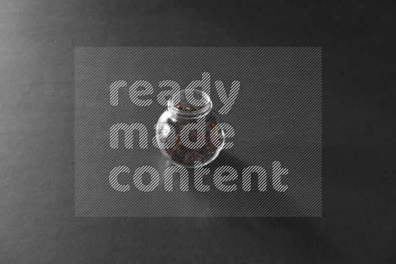 A glass spice jar full of cloves on black flooring