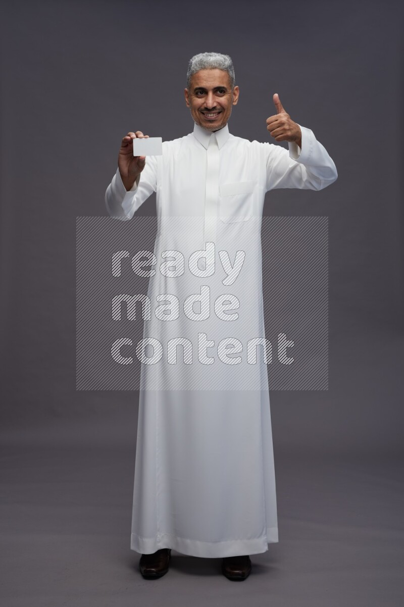 Saudi man wearing thob standing holding ATM card on gray background