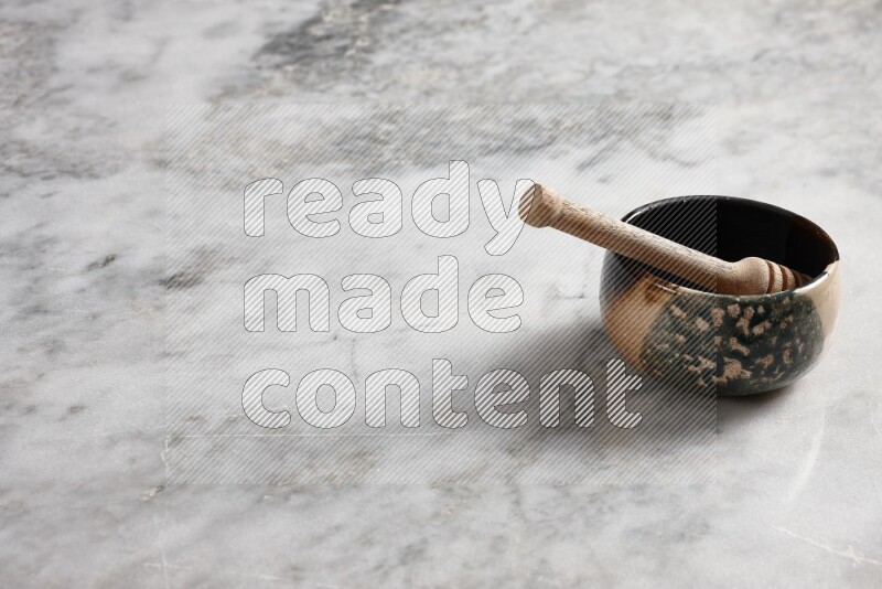 وعاء فخاري متعدد الألوان مع ملعقة عسل خشبية بداخله على خلفية من الرخام الرمادي