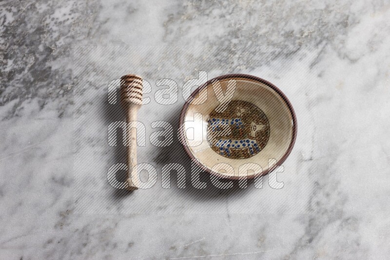 Decorative pottery plate with wooden honey dipper on the side on grey marble background