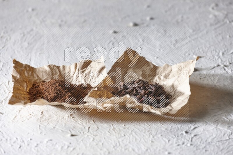 Cloves powder and cloves on 2 crumpled pieces of paper on a textured white flooring