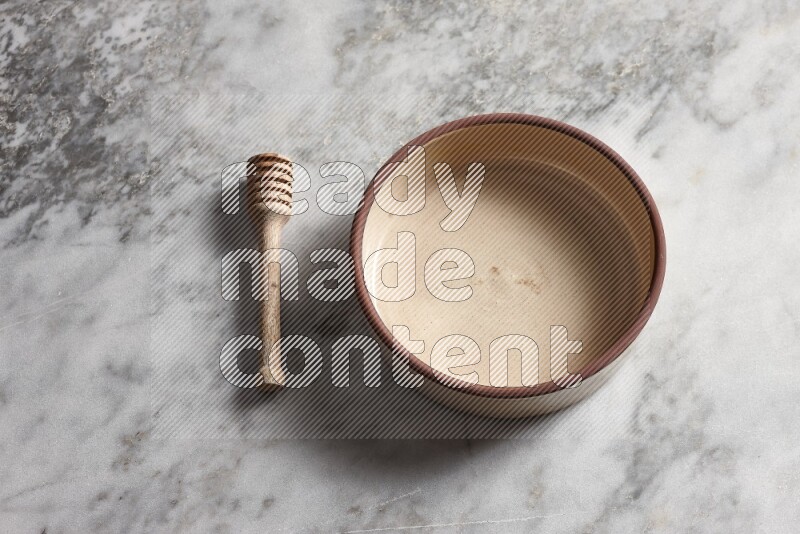 Beige pottery oven bowl with wooden honey dipper on the side on grey marble background