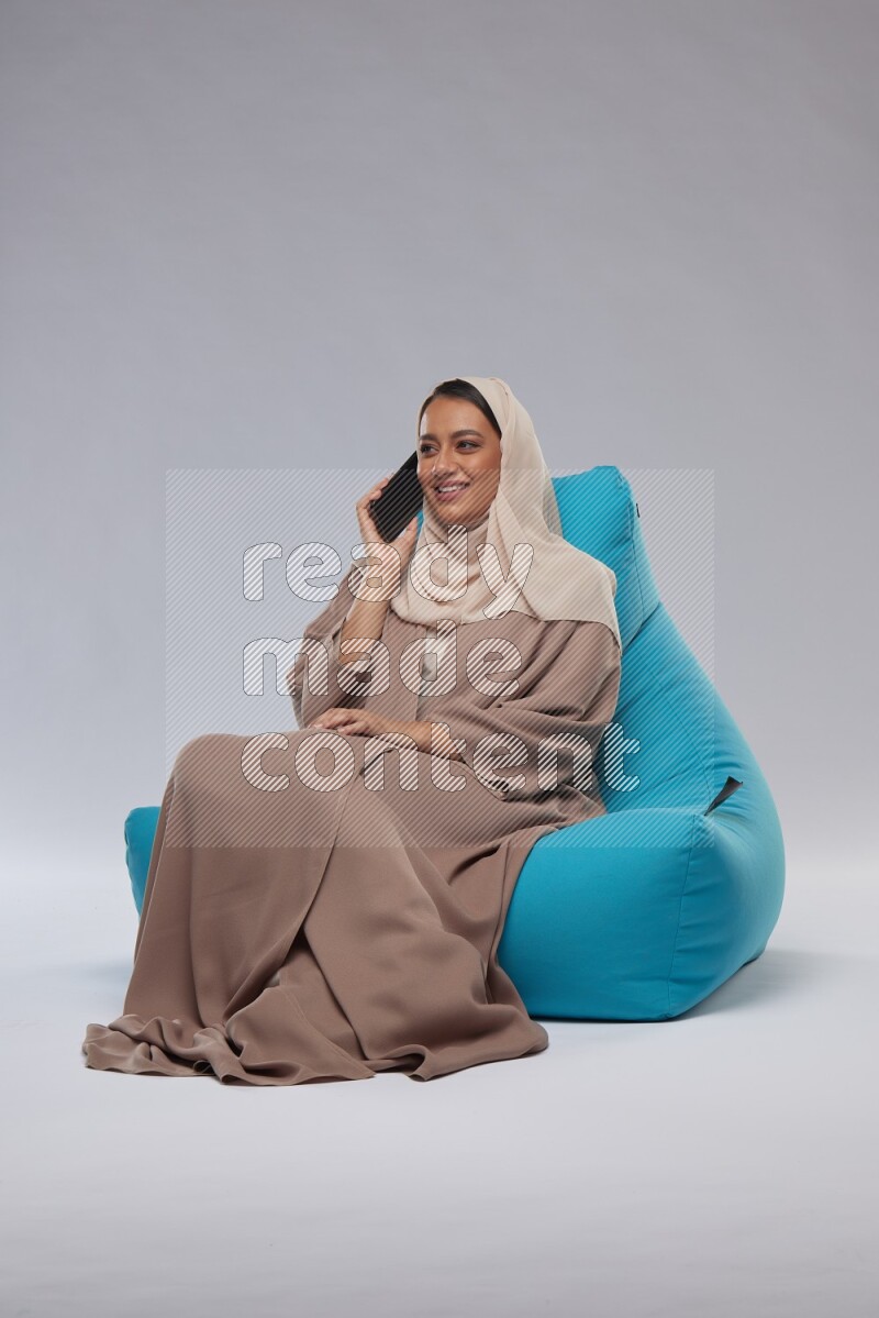 A Saudi woman sitting on a blue beanbag and working on laptop