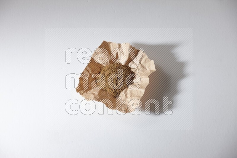 Cumin powder in a crumpled piece of paper on white flooring