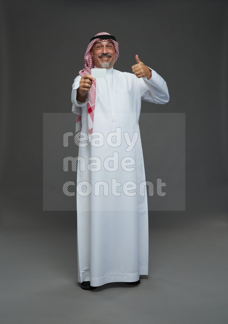 Saudi man with shomag Standing holding ATM card on gray background