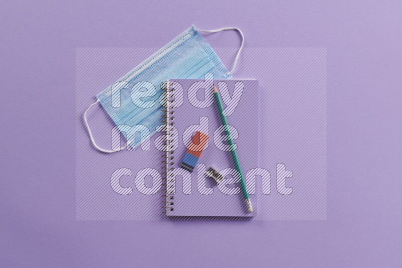 A purple notebook with different school supplies on purple background