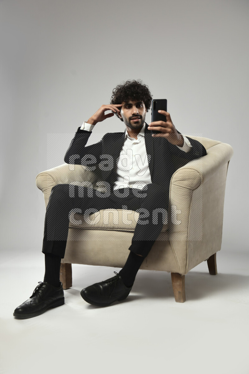 A man wearing formal sitting on a chair browsing on the phone on white background