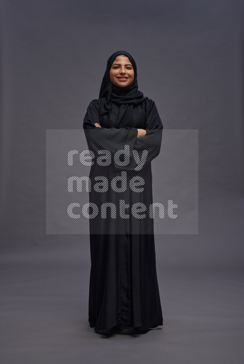 Saudi woman wearing Abaya standing with crossed arms on gray background
