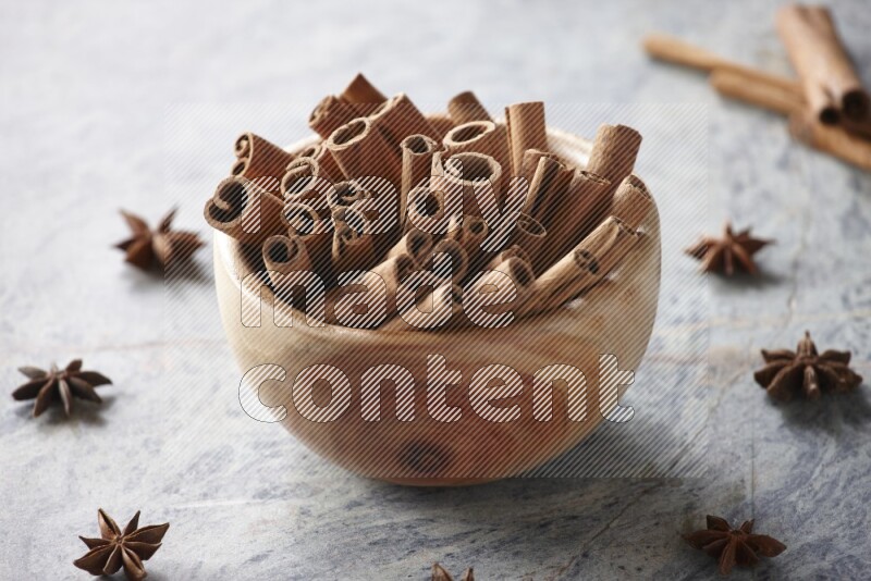 wooden bowl full of cinnamon sticks surrounded by star anis on marble background in different angles