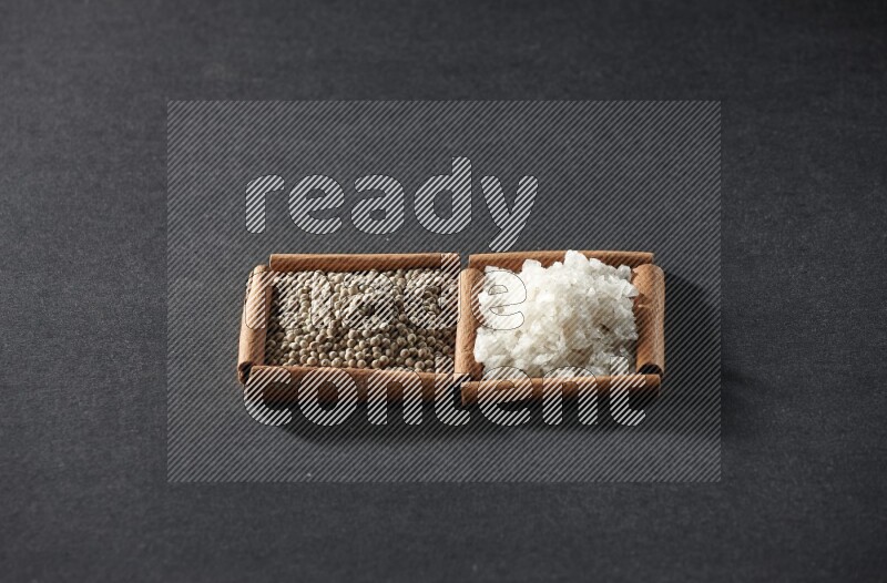 مربعان من أعواد القرفة ممتلئان بحبوب الفلفل الأسود والملح علي خلفية سوداء