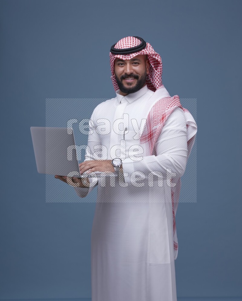 A Saudi man Holding a Laptop on Blue Background wearing Saudi Thob and Shomag