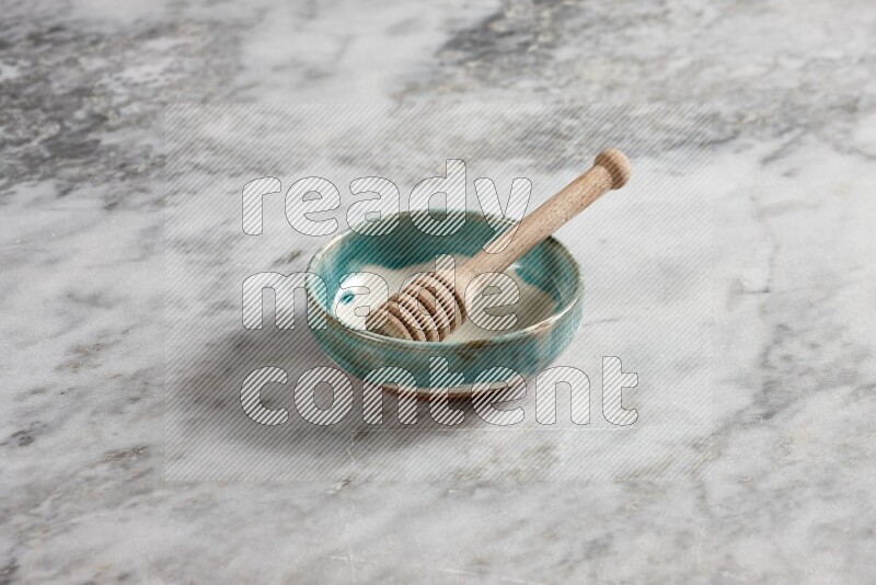Multicolored pottery bowl with wooden honey dipper in it on grey marble background