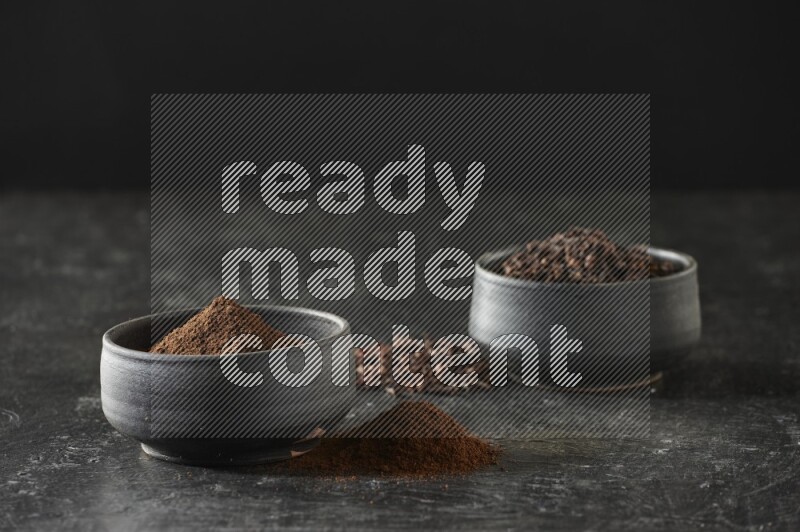 وعاءين من الفخار الأسود أحدهما ممتلئي بحبوب القرنفل والآخر ممتلئ ببودرة القرنفل على خلفية سوداء