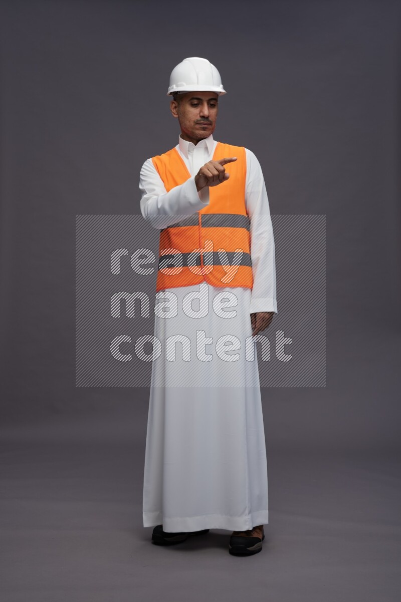 Saudi man wearing thob with engineer vest standing interacting with the camera on gray background