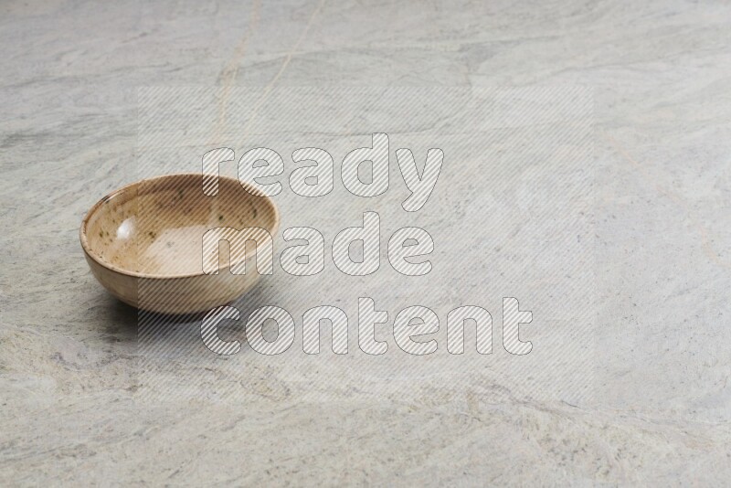 A small beige pottery bowl on grey marble background