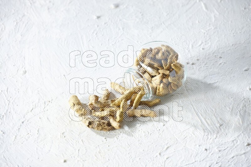 A flipped glass spice jar full of dried turmeric fingers and fell out it on textured white flooring