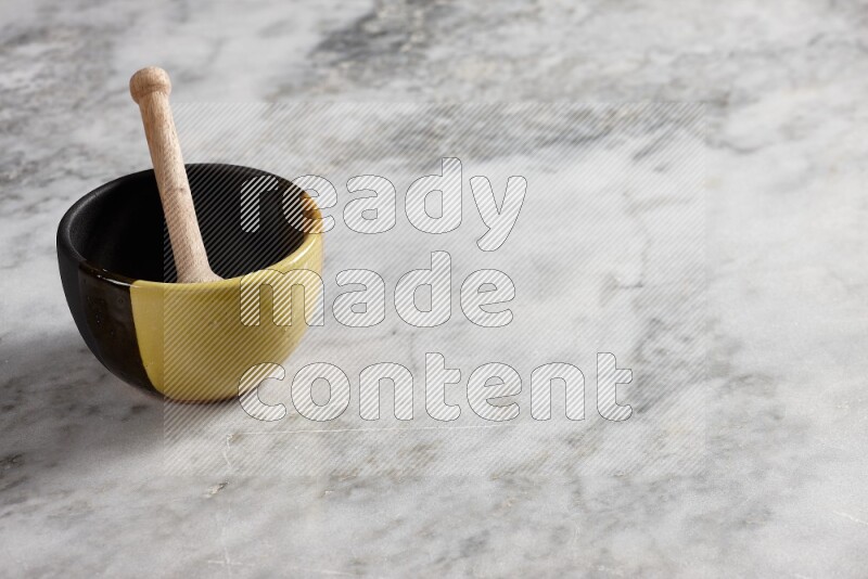 Multicolored pottery bowl with wooden honey dipper in it on grey marble background