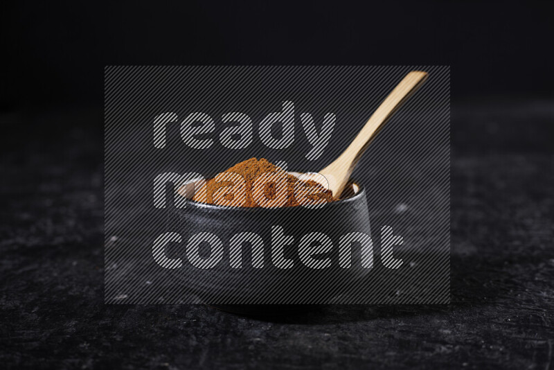 A black pottery bowl full of ground paprika powder on black background