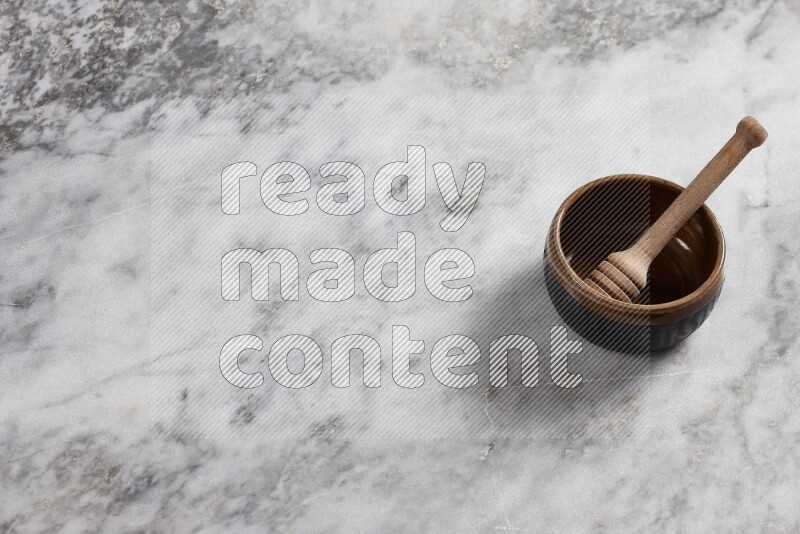 Multicolored pottery bowl with wooden honey dipper in it on grey marble background